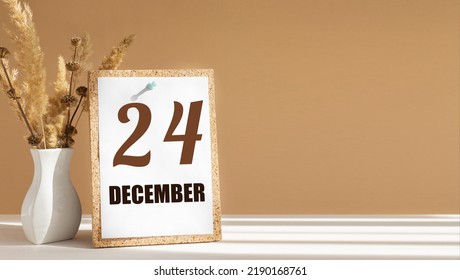 december 24. 24th day of month, calendar date.White vase with dead wood next to cork board with numbers. White-beige background with striped shadow. Concept of day of year, time planner, winter month.