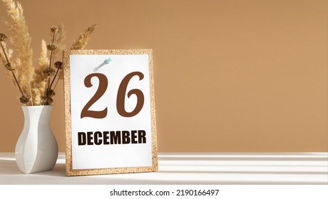 december 26. 26th day of month, calendar date.White vase with dead wood next to cork board with numbers. White-beige background with striped shadow. Concept of day of year, time planner, winter month