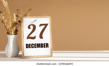 december 27. 27th day of month, calendar date.White vase with dead wood next to cork board with numbers. White-beige background with striped shadow. Concept of day of year, time planner, winter month
