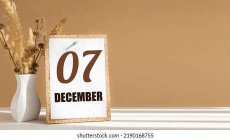 december 7. 7th day of month, calendar date.White vase with dead wood next to cork board with numbers. White-beige background with striped shadow. Concept of day of year, time planner, winter month.