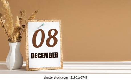 december 8. 8th day of month, calendar date.White vase with dead wood next to cork board with numbers. White-beige background with striped shadow. Concept of day of year, time planner, winter month.
