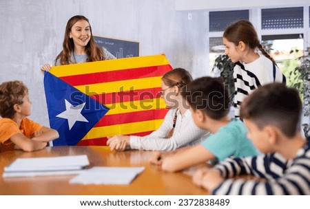 Decent teacher showing Catalonia flag to group of preteen schoolchildren in classroom during lesson
