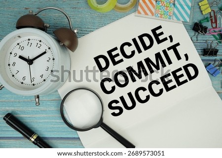 Decide, Commit, Succeed text written on notepad with alarm clock and magnifying glass flat lay on wooden background
