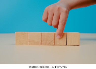 Decision making and selection concept. Hand pointing at a blank wooden cube on blue background, symbolizing choice, priority, strategy, focus, planning, and business decision process.