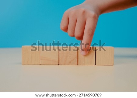 Decision making and selection concept. Hand pointing at a blank wooden cube on blue background, symbolizing choice, priority, strategy, focus, planning, and business decision process.