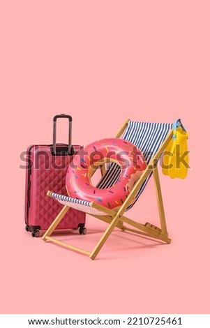 Deck chair, suitcase and beach accessories on pink background