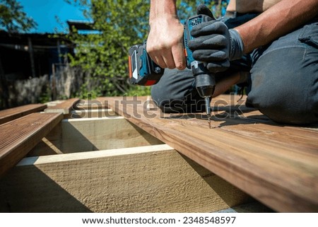 Deck construction, builder hand with electric screwdriver installing impregnated wooden boards