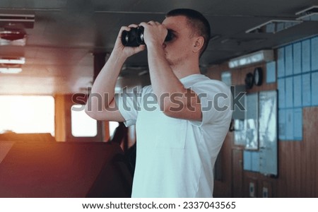 Deck officer on the bridge during navigational watch at sea. Offshore technician. Seafarer. Seaman. Navigator. A man in the wheelhouse during watchkeeping duty. Look out with binoculars.