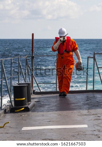 Deck Officer on ship , wearing personal protective equipment, holds VHF radio in hands.	