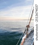 Deck and ropes, rigging on a wooden tall ship sail yacht. Lines coiled on tall ship. Sailing on a sailboat across calm waters with mountains in the background during evening light on a serene lake.