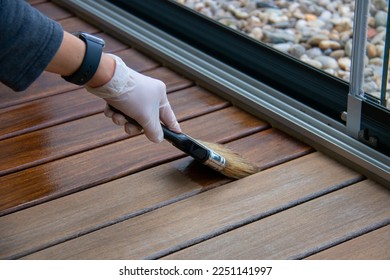 Deck staining, worker applying deck oil on decking boards with paint brush, hardwood terrace renovation - Shutterstock ID 2251141997
