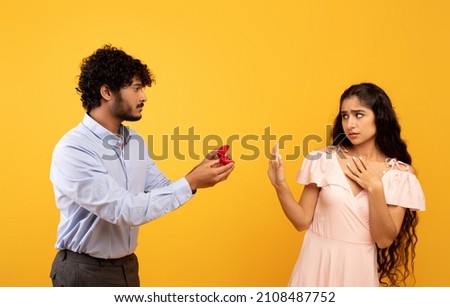 Declining proposal. Indian woman refusing to take engagement ring rejecting boyfriend, standing over yellow background, studio shot. She said no