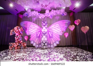 Decor of the girl's first birthday. Beautiful pink photo zone for one year old baby girl with big paper and balls butterfly. big letter number one with pink balloons. Happy Birthday party