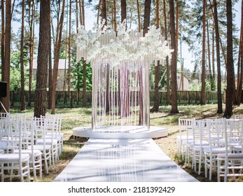 The Decor Of The Wedding Altar And The Road To It In White At An Outdoor Ceremony In A Pine Forest. White Flowers, Ribbons, Glass. On The Sides Are White Chairs For Guests.