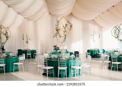 The decor of the wedding banquet hall with tables in emerald green, white drapery on the ceiling, gold geometric decorative elements. - Shutterstock ID 2192815575