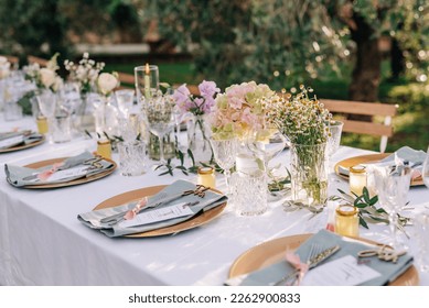 The decor of the wedding dinner in the olive grove. Corner table is decorated with flowers, roses and hydrangeas. Wedding banquet in light white and pink colors