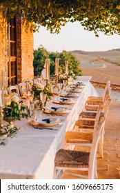 Decor Of A Wedding Table For Dinner In Tuscany In The Summer At Sunset In The Field. Rustic Elegant Italian Wedding Decor With Natural Flowers, Olives And Candles.