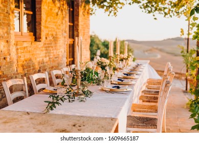 Decor of a wedding table for dinner in Tuscany in the summer at sunset in the field. Rustic elegant Italian wedding decor with natural flowers, olives and candles.