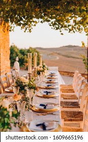 Decor Of A Wedding Table For Dinner In Tuscany In The Summer At Sunset In The Field. Rustic Elegant Italian Wedding Decor With Natural Flowers, Olives And Candles.