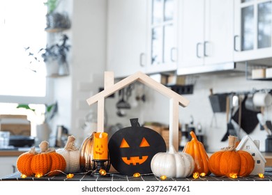 Decor of white classic kitchen with pumpkins, garlands, jack latern for Halloween and harvest with figurine of house. Autumn mood in home interior, modern loft style. real estate, insurance, mortgage