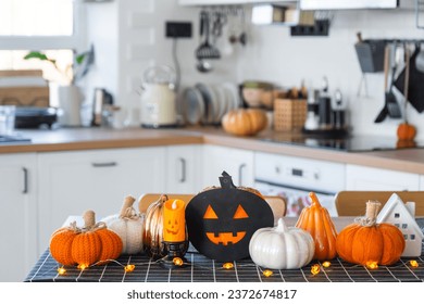 Decor of white classic kitchen with pumpkins, garlands, jack latern for Halloween and harvest with figurine of house. Autumn mood in home interior, modern loft style. real estate, insurance, mortgage