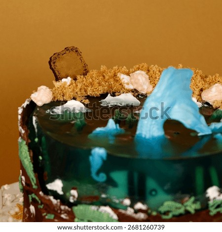 Decorated cake with ocean theme featuring transparent blue gelatin water effect, fondant whales, coral, and detailed landscape decoration. The whimsical design conveys artistic confectionery