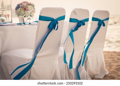 Decorated Chairs At Dining Table On The Beach For Special Guests At A Wedding Ceremony.