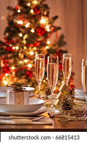 A Decorated Christmas Dining Table With Champagne Glasses And Christmas Tree In Background