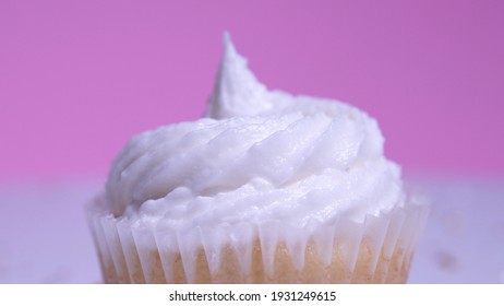 Decorated colourful cupcake for the holiday, shallow depth of field. Close up macro focus on the iced muffin. Pink background. Presentation of delicious desserts at anniversary or birthday.