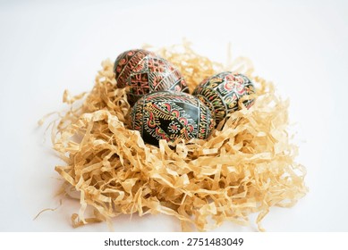 Decorated Easter eggs placed in small paper nest on white background. Traditional pysanka eggs symbolizing spring renewal and Easter celebration.