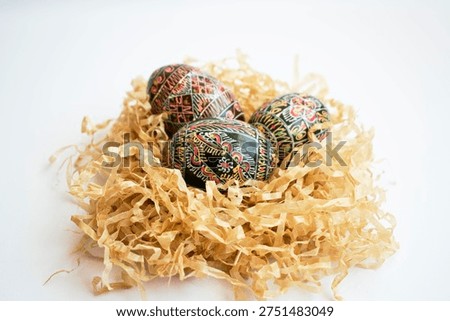 Decorated Easter eggs placed in small paper nest on white background. Traditional pysanka eggs symbolizing spring renewal and Easter celebration.