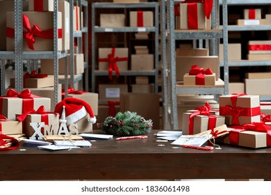 Decorated Merry Christmas table with gifts boxes in warehouse interior background. Many presents wrapped with red ribbons and letters on desk in storage. Xmas postal shipping delivery concept.