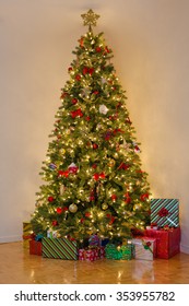 Decorated Pine Tree With Many Presents Under It. Room Lit Only By Yellow Christmas Tree Lights. Classical Style Decor: Main Colors Are Red, Yellow And Green.