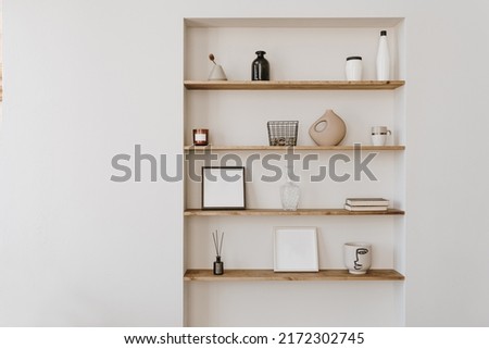 Decorated shelf on white wall. Aesthetic luxury minimalist home interior design decoration. Elegant Scandinavian, hygge style interior. Picture frames, fragrance, vase, books, candle