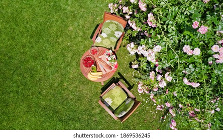 Decorated table with bread, strawberry and fruits in beautiful summer rose garden, aerial top view of romantic date table food setting for two from above
