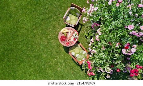 Decorated Table With Bread, Strawberry And Fruits In Beautiful Summer Rose Garden, Aerial Drone View Of Romantic Date Table Food Setting For Two From Above