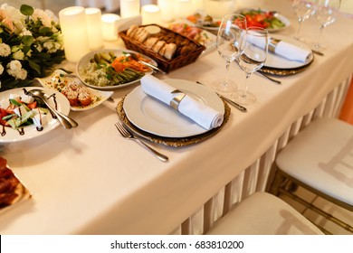 Decorated table, a plate of neatly arranged napkin, fork and knife. Top view of the beautifully decorated table with white plates, crystal glasses, linen napkin and cutlery on luxurious tablecloths.