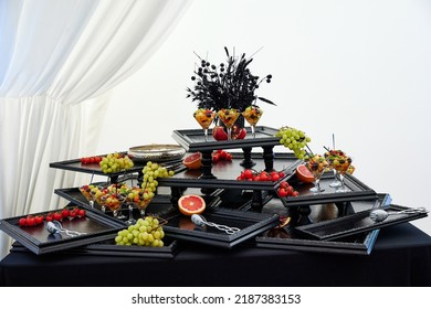Decorated trays with fresh organic fruits put on black table in restaurant premise. Diversity of healthy food served for guests against white curtain closeup - Shutterstock ID 2187383153