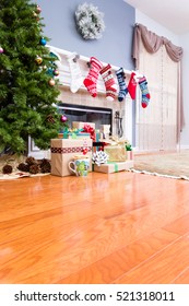 Decorated Upmarket Home At Christmas With Colorful Stockings On The Mantelpiece, A Tree And Pile Of Colorful Gifts, Low Angle View With Copy Space On The Hardwood Floor