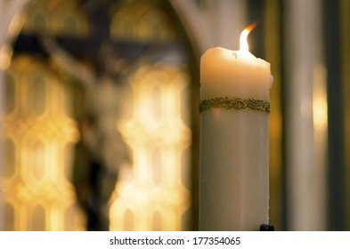 Decorated White Candle Burning Inside A Catholic With The Image Of Christ Behind Church