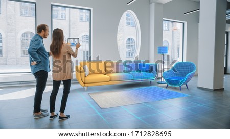 Decorating Apartment: Lovely Young Couple Use Digital Tablet with Augmented Reality Interior Design Software to Choose 3D Furniture for their Home. People Pick Sofa, Table and Lighting for Living Room Stockfoto © 