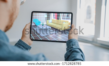 Decorating Apartment: Man Holding Digital Tablet with AR Interior Design Software Chooses 3D Furniture for Home. Man is Choosing Sofa, Table for Living Room. Over Shoulder Screen Shot with 3D Render Stok fotoğraf © 