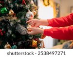 Decorating Christmas tree with colorful ornaments brings joy and festive spirit. hands carefully place golden bauble among vibrant decorations, creating warm holiday atmosphere.