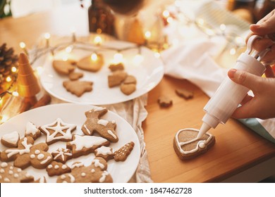 Decorating gingerbread cookies with icing on rustic table with lights. Christmas holiday tradition and advent. Hands decorating baked christmas cookies with sugar frosting. Family time - Powered by Shutterstock