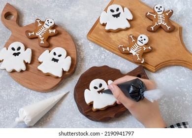Decorating Halloween gingerbreads of ghosts and skeletons with frosting. Girl holds pastry bag with black icing and decorates gingerbread ghost