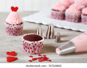 Decorating red velvet cupcakes with pink frosting and red hearts for Valentine's day.