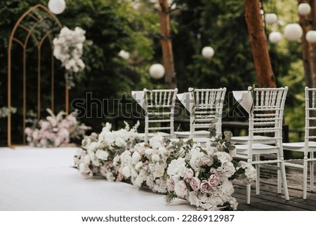 Decoration of chairs for guests with flower arrangement for the wedding ceremony in the green forest .