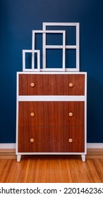 Decoration Home Interior. Empty White Frames On Top Of An Accent Dresser Against A Blue Wall On Hardwood Floors