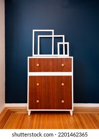 Decoration Home Interior. Empty White Frames On Top Of An Accent Dresser Against A Blue Wall On Hardwood Floors