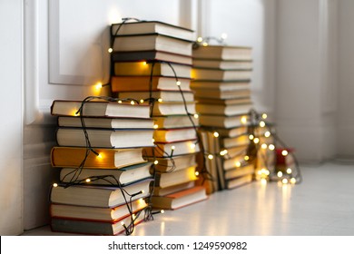 Decoration of the house in Scandinavian style. Stacks of books on the floor with a glowing garland. Christmas decor. Background for Christmas card. Soft focus - Powered by Shutterstock